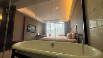 Una habitación de hotel moderna con una bañera grande, un televisor y un ventanal con cortinas.