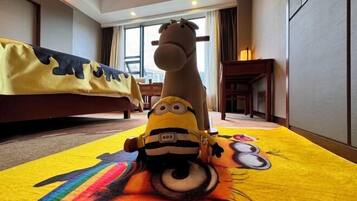 A hotel room with a large bed, a Minion plush toy on a colorful rug, and a giraffe statue.