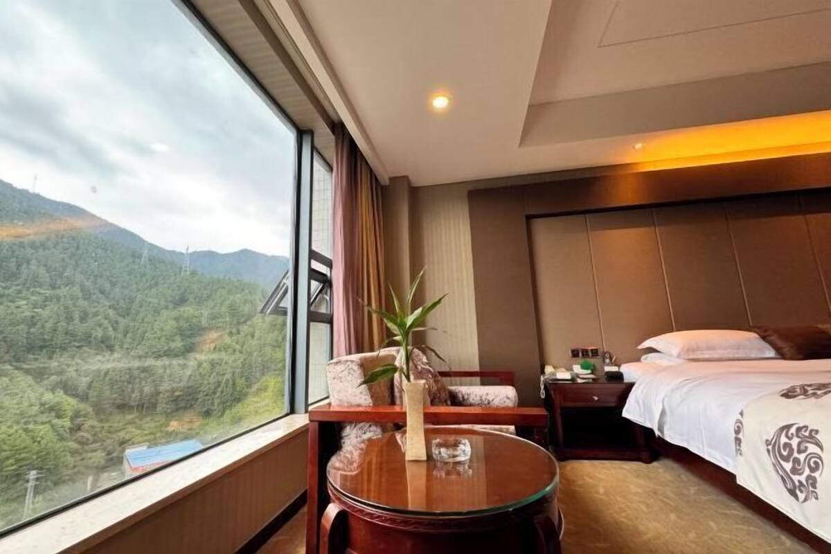 A hotel room with a large window offering a view of a forested mountain range.