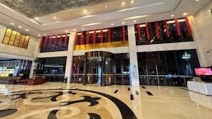 A spacious lobby with a large, ornate floor design, a glass elevator, and red lanterns.