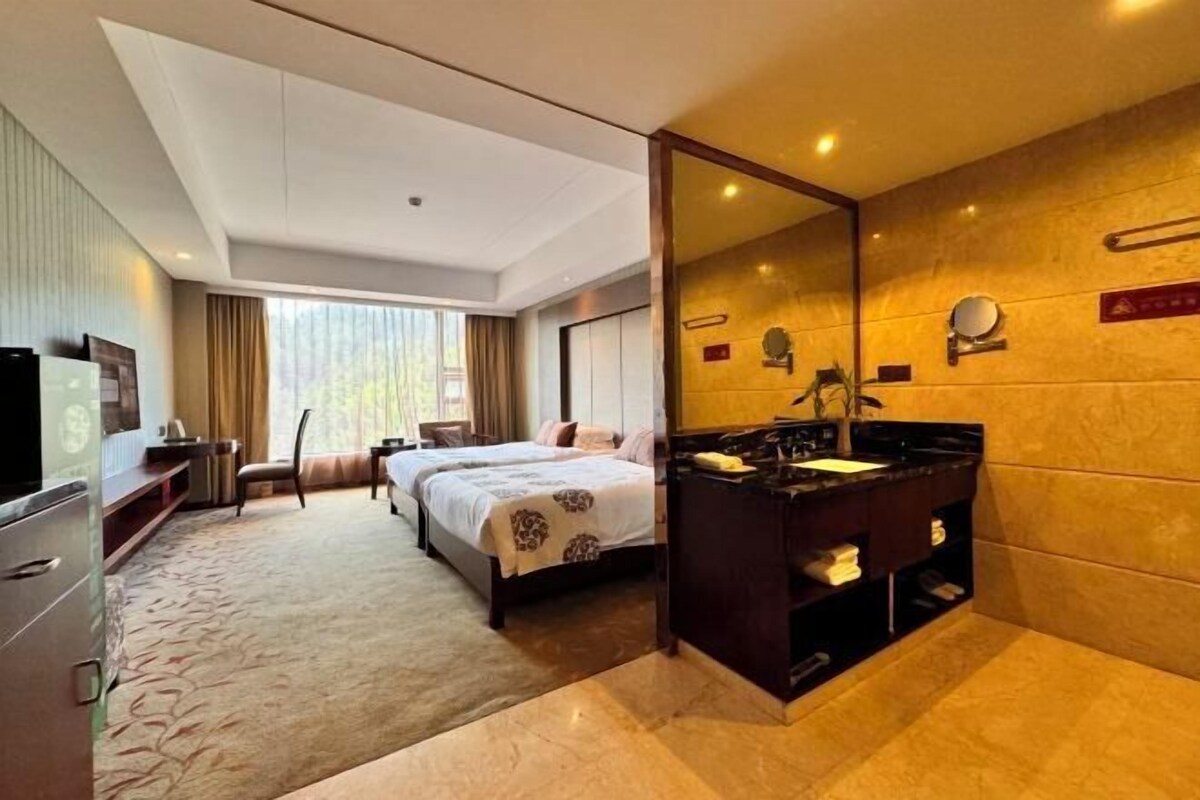 A hotel room with two beds, a large mirror, a vanity with a sink, and a television.
