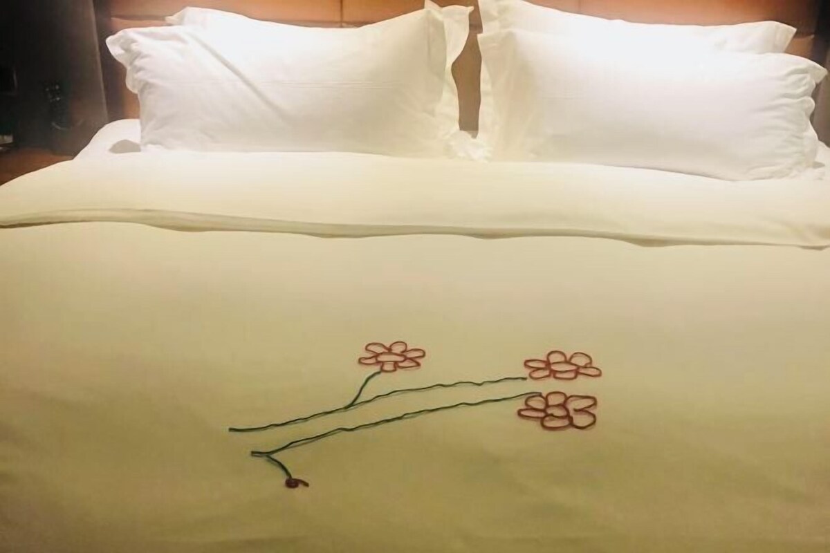 A bed with white bedding and a decorative embroidered branch with flowers.