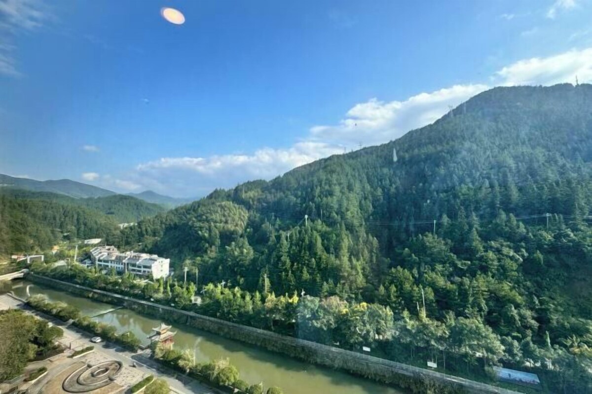 A river running through a valley with a bridge, surrounded by dense forest and hills.
