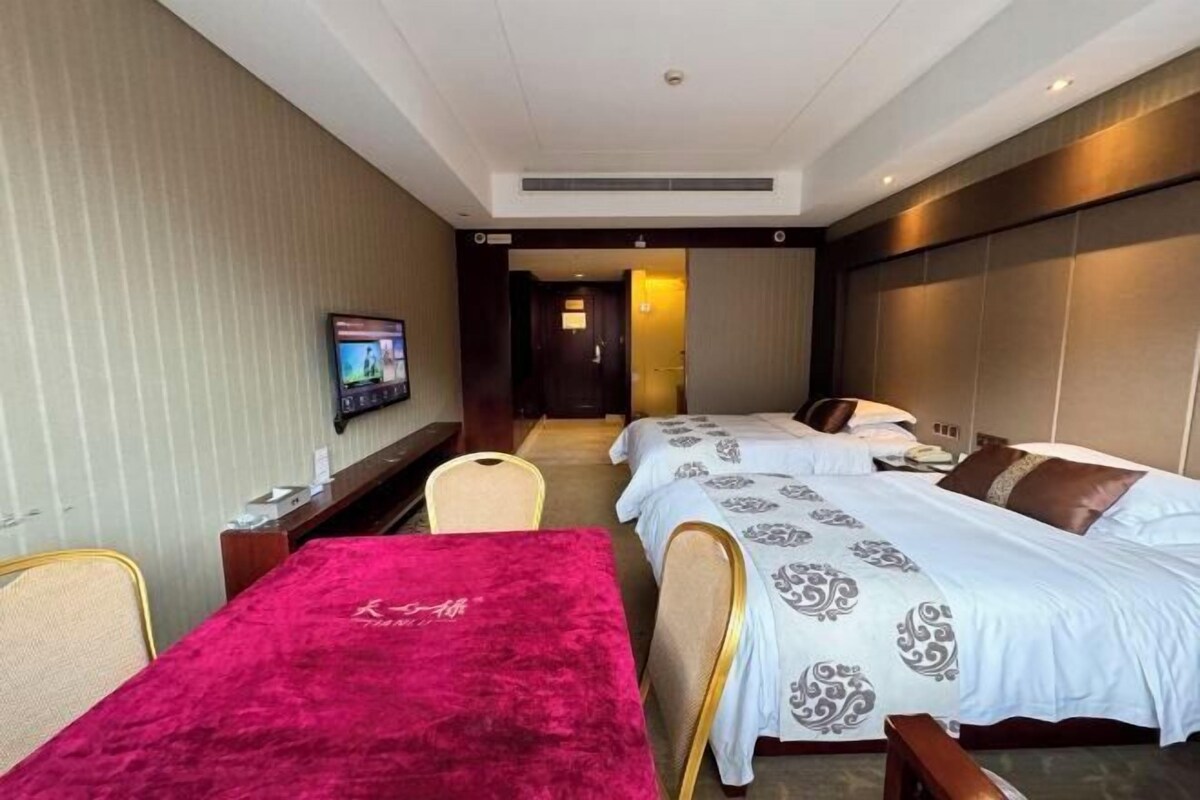 A hotel room with two beds, a TV, a desk, and a chair.