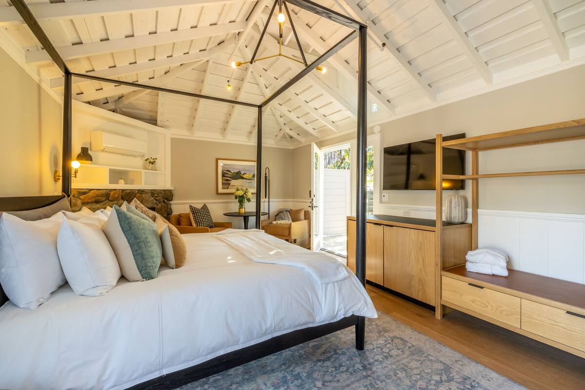 A bedroom with a four-poster bed, a wooden desk, and a stone fireplace.