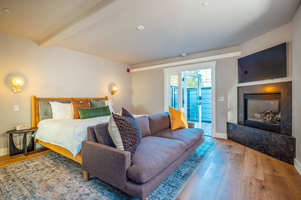 A modern bedroom with a large bed, a sofa, a fireplace, and a TV.