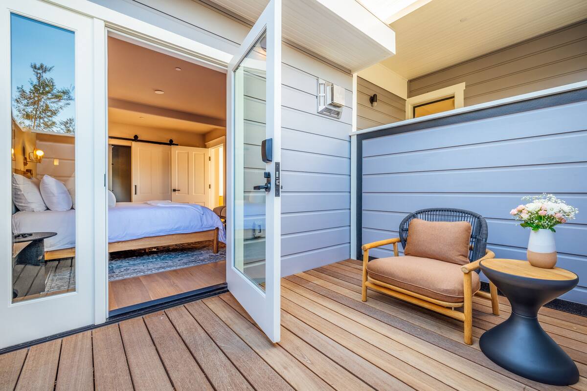 An open sliding door leading to a bedroom with a bed, a chair, and a small table.