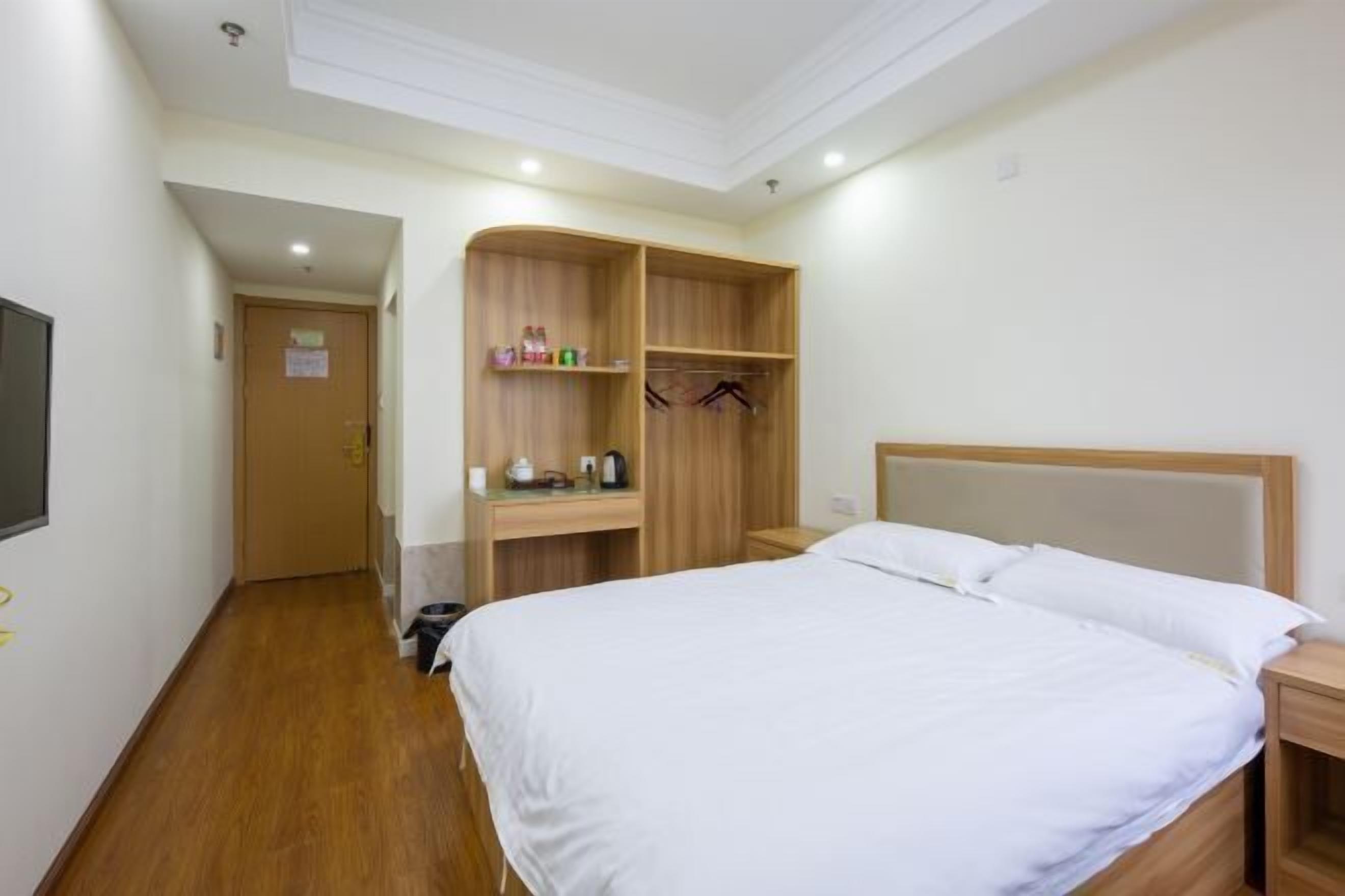A hotel room with a large bed, wooden wardrobe, and a small desk with a chair.