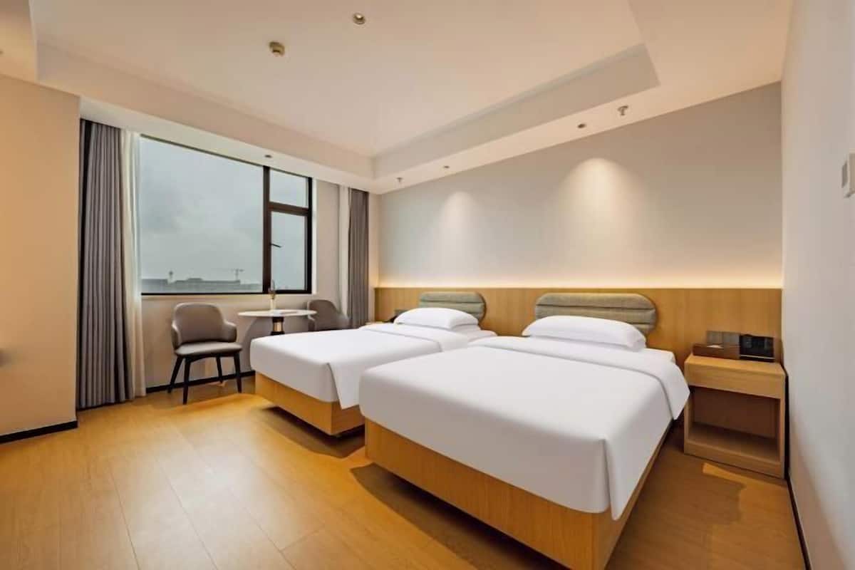 Ein Hotelzimmer mit zwei Betten, einem Schreibtisch, einem Stuhl und einem großen Fenster.