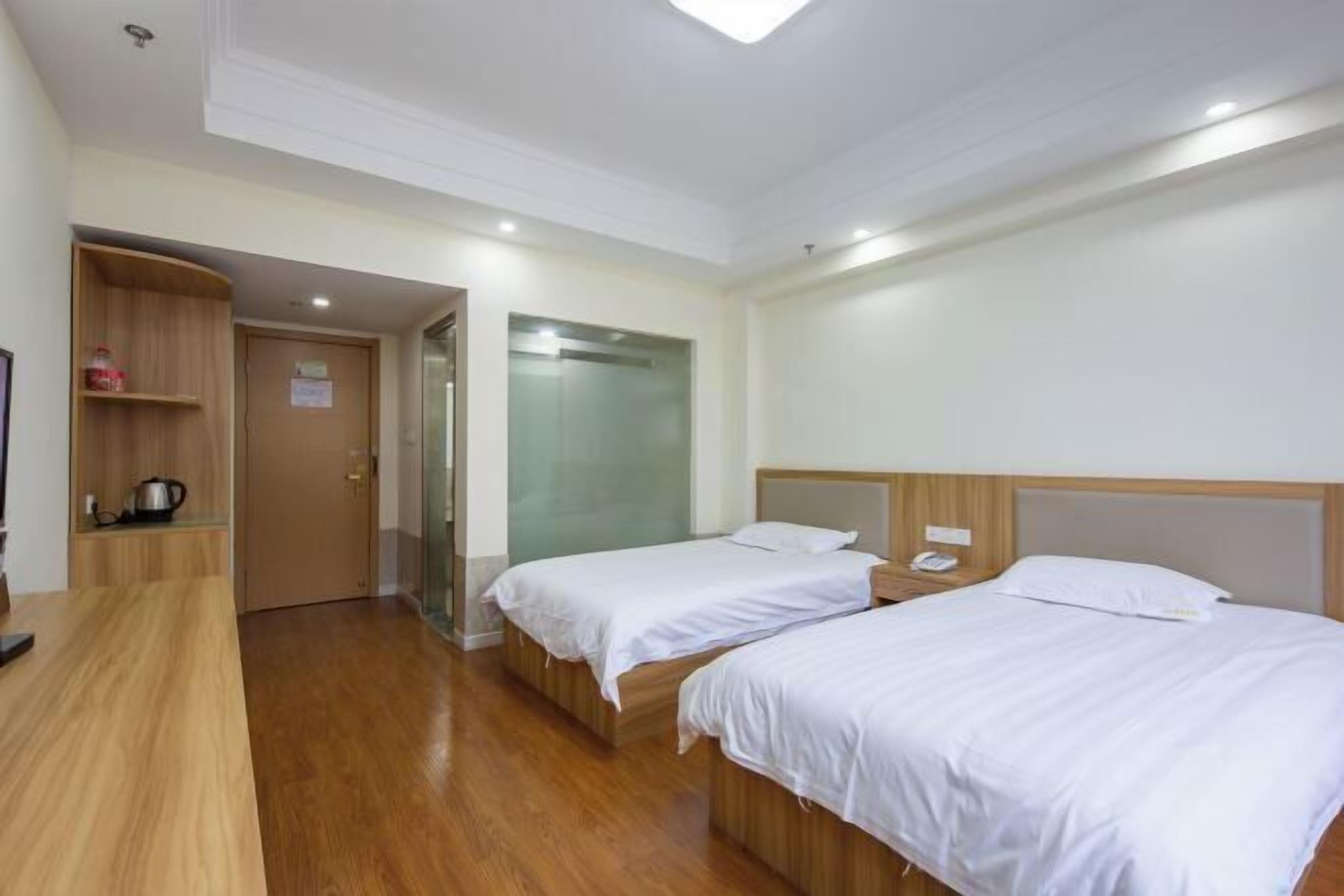 A hotel room with two beds, a wooden desk, a glass shower, and a wooden wardrobe.