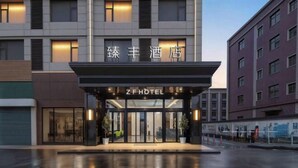 A hotel entrance with a glass facade, a sign reading 'ZFHOTEL,' and a modern building facade in the background. - Zhenfeng Business Hotel (Ningbo)