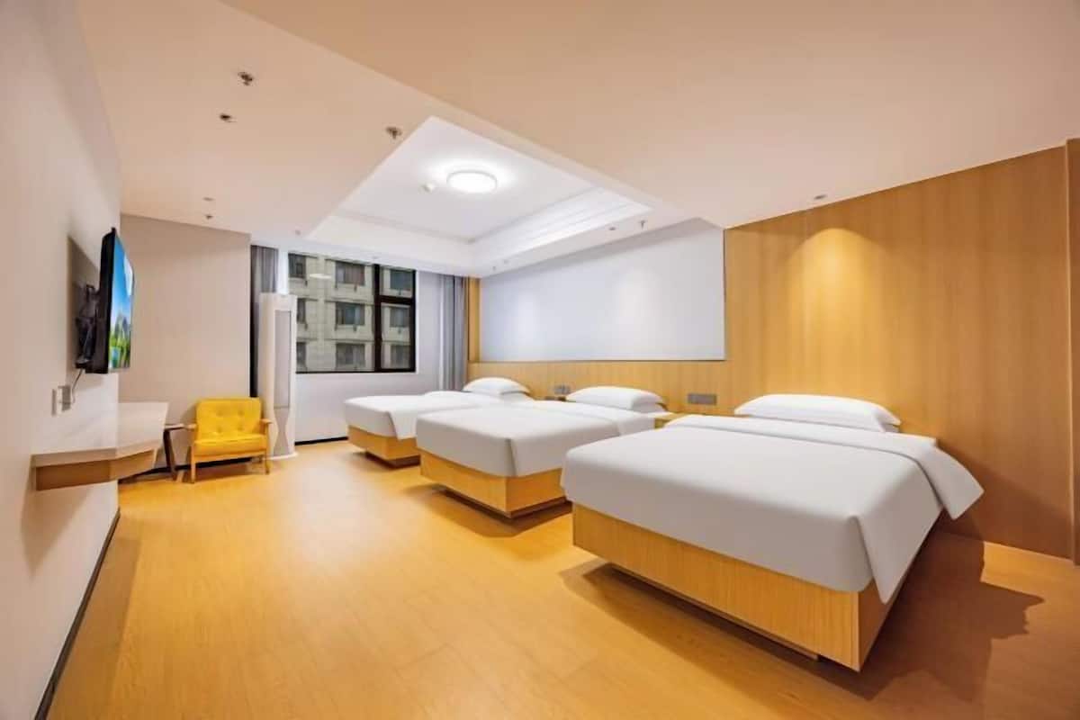 Ein Hotelzimmer mit drei Betten, einem kleinen Schreibtisch, einem Stuhl und einem großen Fenster.