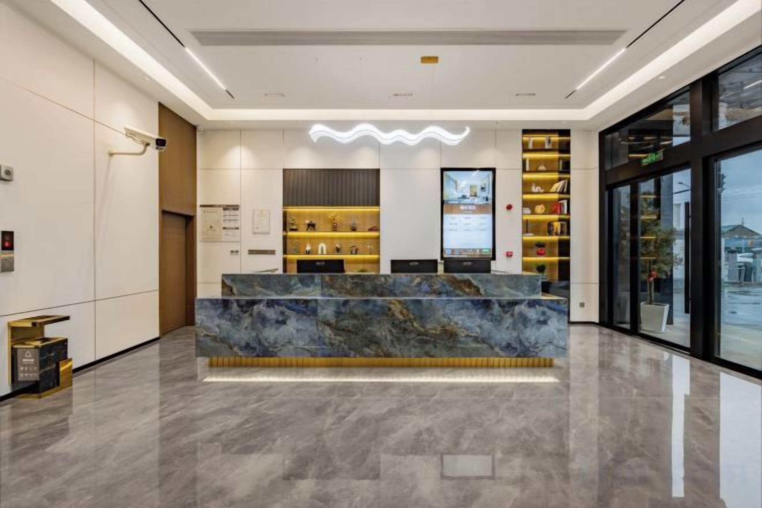 Una moderna zona de recepción con mostrador de mármol, un panel informativo digital y vistas al exterior a través de amplios ventanales.
