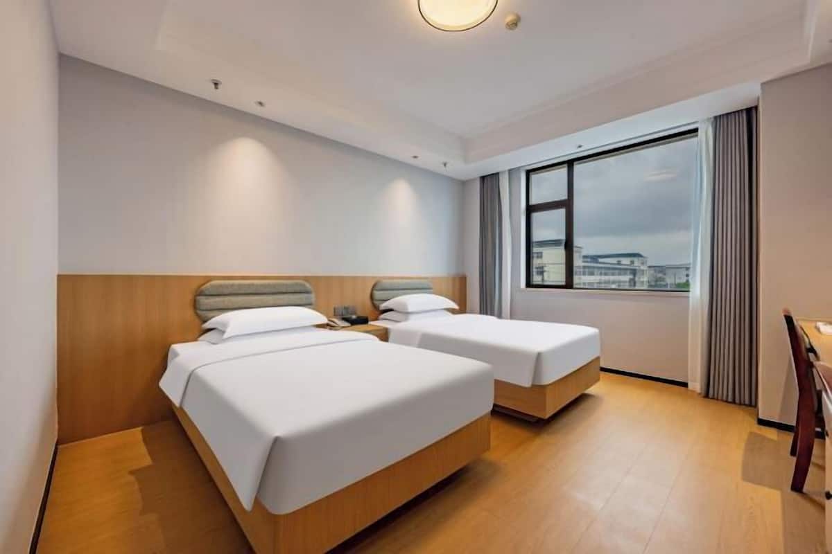 Ein Hotelzimmer mit zwei Betten, einem Holzkopfende, einem großen Fenster mit Blick auf die Stadt und einem Schreibtisch mit Stuhl.
