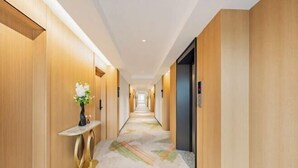 A hotel hallway with wooden walls, a central console table with a vase, and a patterned carpet. - Zhenfeng Business Hotel (Ningbo)