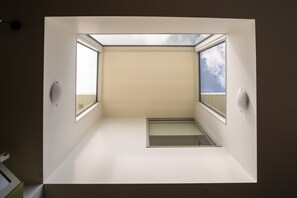 Una habitación con tragaluces, un ventanal pequeño y estantería empotrada.