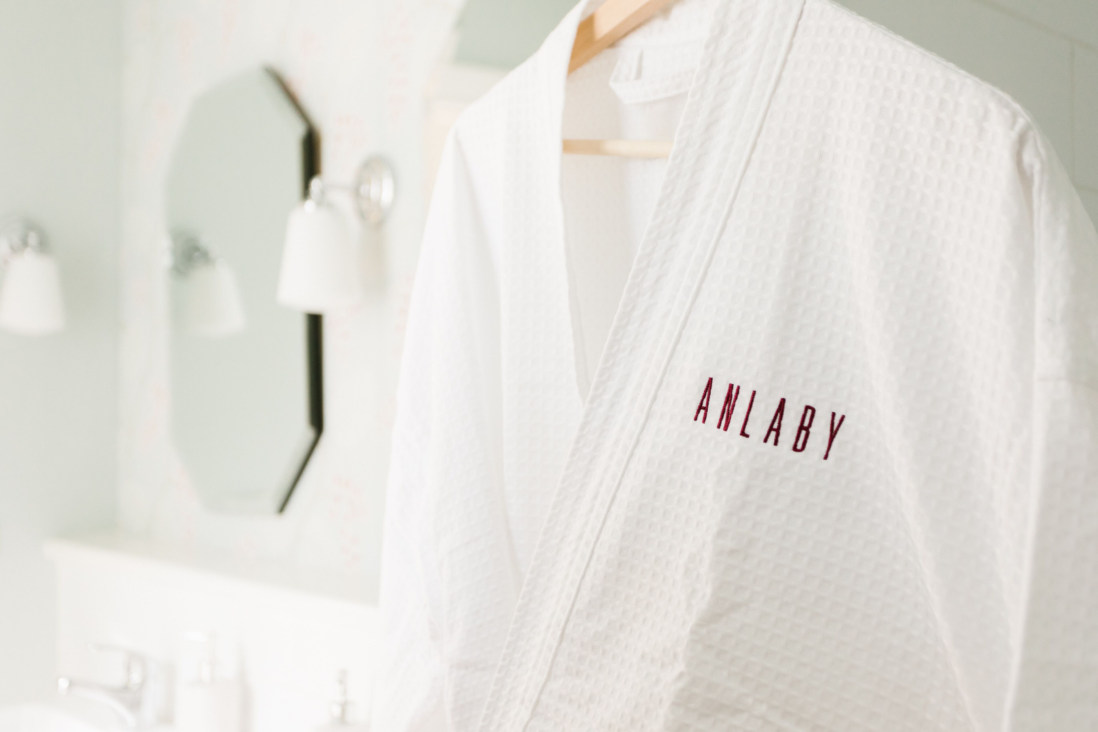 A white robe with "ANLABY" embroidered on it hanging on a wooden hanger.