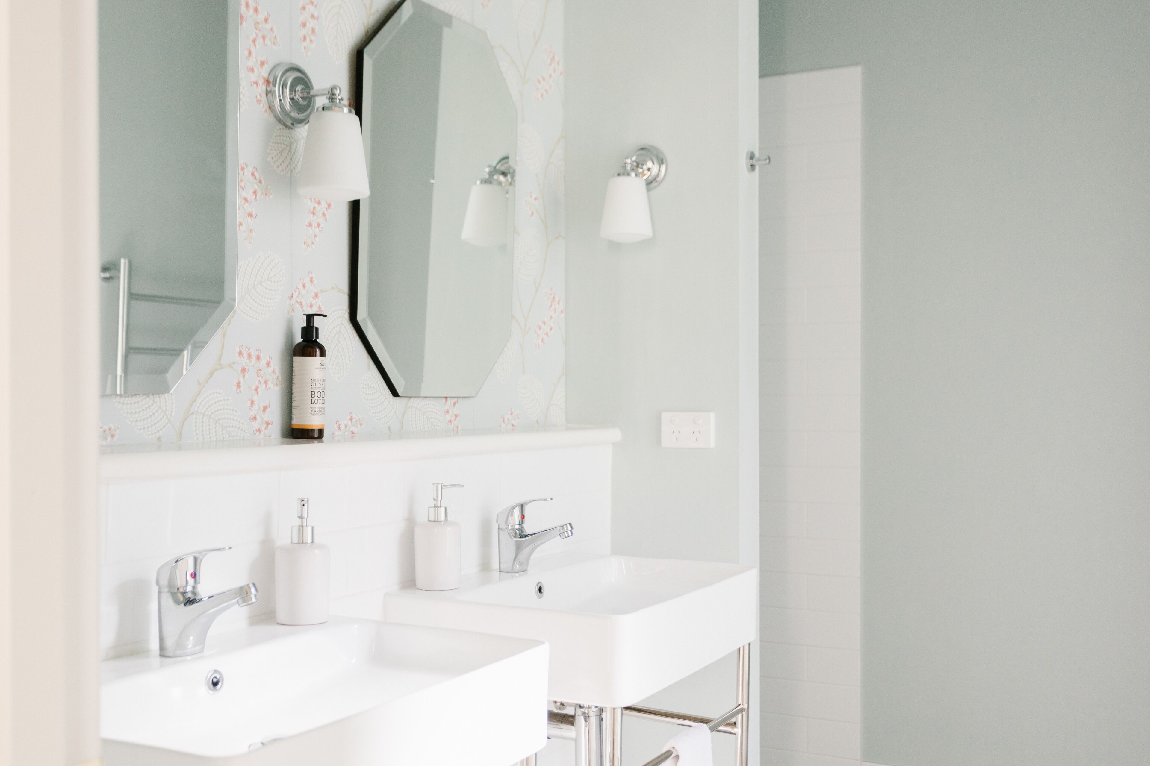 Une salle de bain moderne avec deux vasques blanches, un grand miroir et des luminaires fixés au mur.