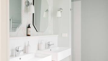 Un bagno moderno con due lavabi bianchi, uno specchio grande e lampade a parete.