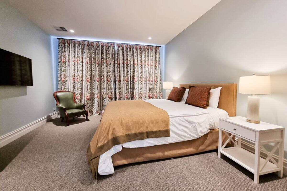 A bedroom with a bed, a nightstand, a chair, and a TV mounted on the wall.