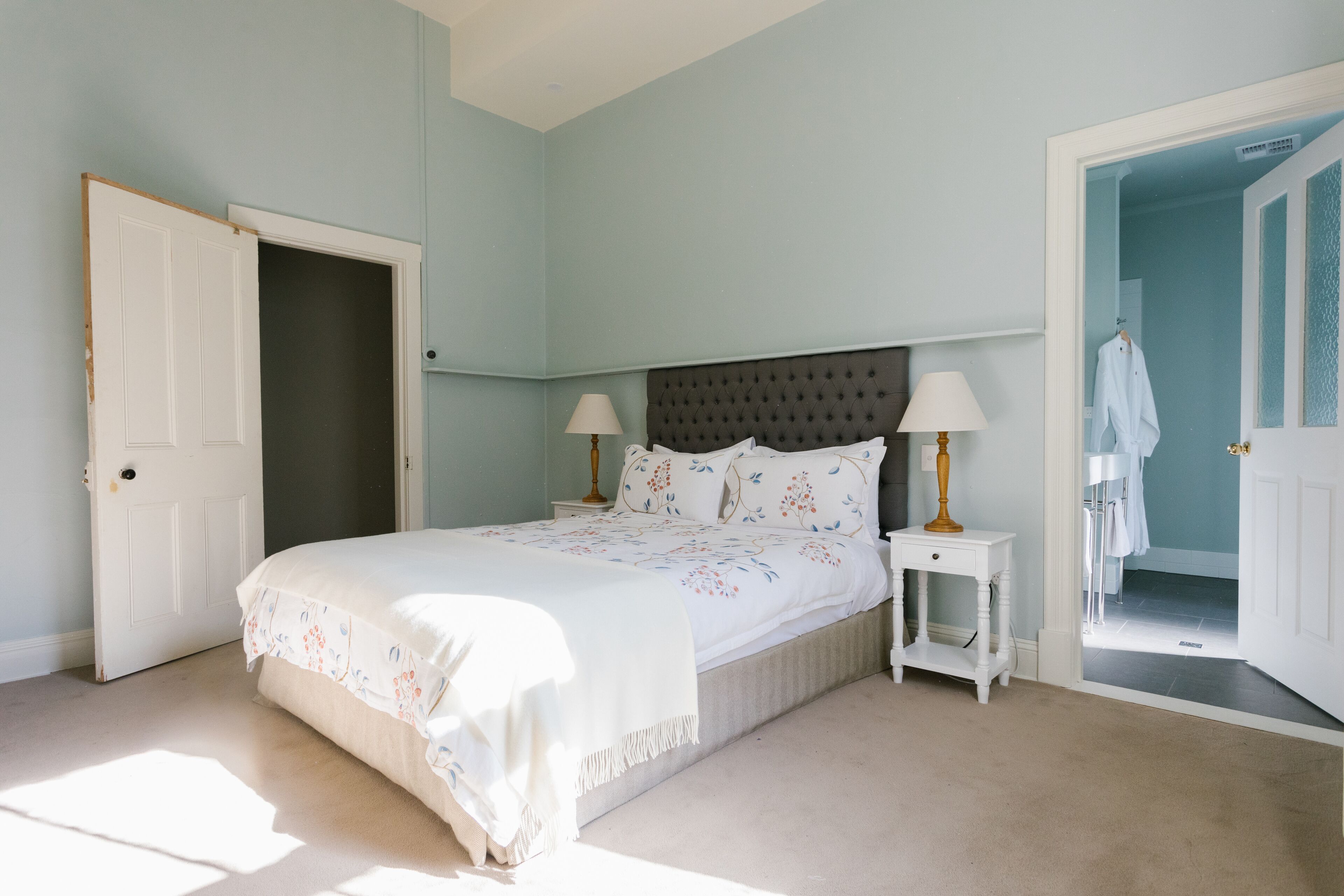 Un dormitorio con una cama, dos mesitas de noche y una puerta que da a otra habitación.