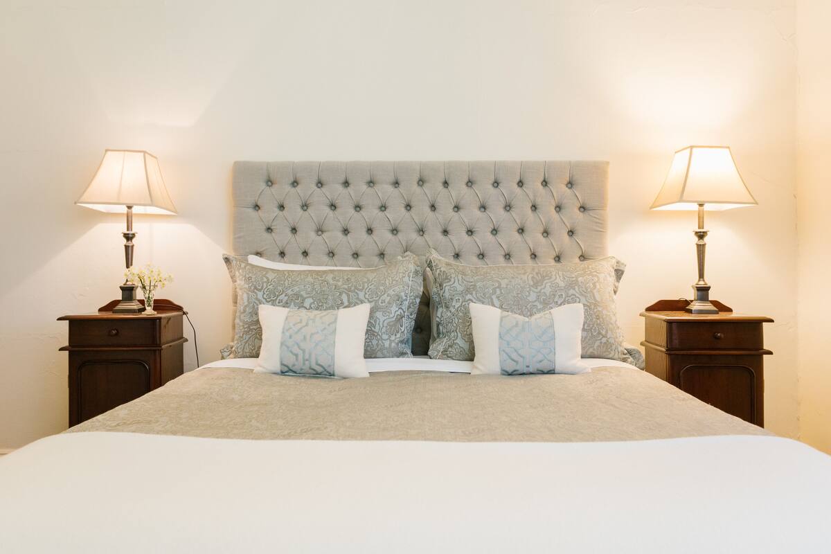 A neatly made bed with a tufted headboard, two bedside tables with lamps, and patterned pillows.