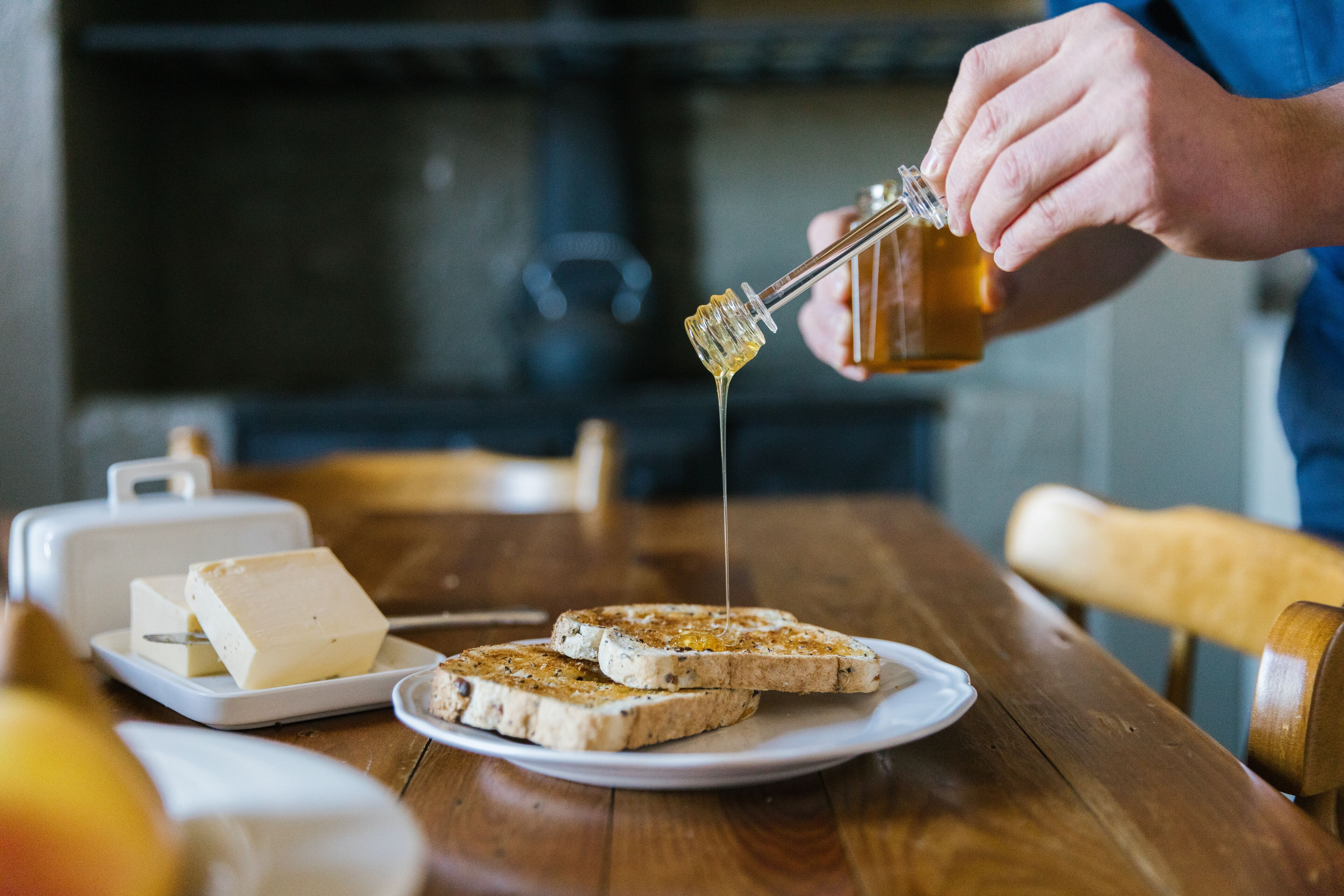 A person pouring honey over toast on a plate.