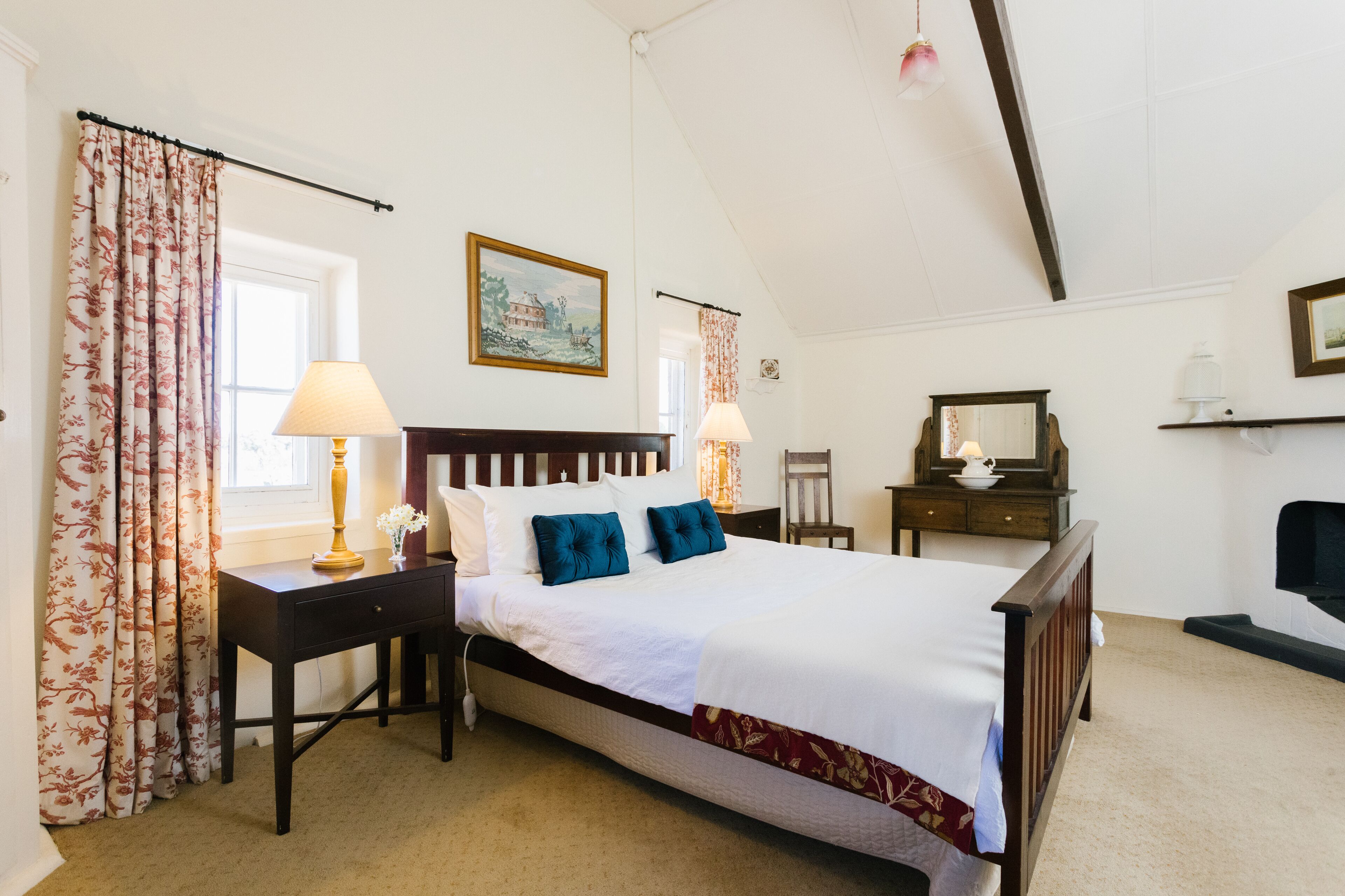 Une chambre à coucher avec un grand lit, une table de chevet, une commode, un miroir et une fenêtre avec des rideaux.