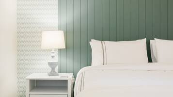 A neatly made bed with white linens and pillows, a bedside table with a lamp, and a patterned wallpaper on the left wall.