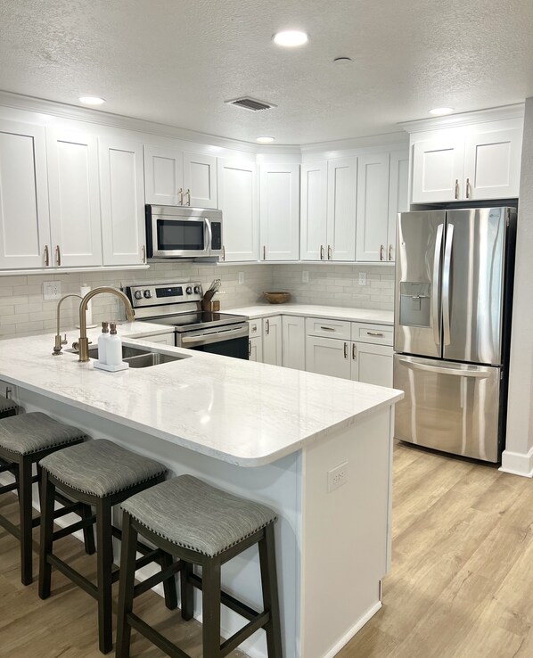 A modern kitchen with white cabinetry, stainless steel appliances, a large island with bar stools, and a wooden floor.
