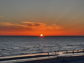 A sunset over the ocean with a beach in the foreground.