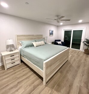 A bedroom with a bed, nightstands, a ceiling fan, and a sliding glass door.