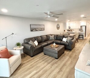 A modern living room with a sectional sofa, ottoman, and a dining area with a bar.