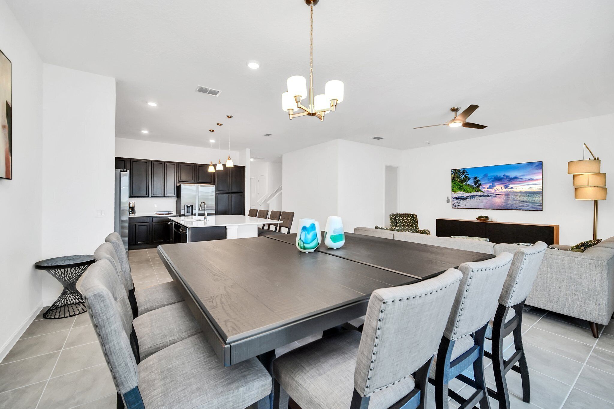 Une cuisine moderne avec des meubles de couleur sombre, un îlot central et un coin repas comprenant une grande table et des chaises.