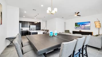 Une cuisine moderne avec des meubles de couleur sombre, un îlot central et un coin repas comprenant une grande table et des chaises.
