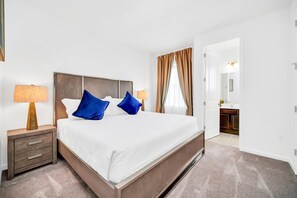 Ein Hotelzimmer mit einem großen Bett, zwei Nachttischen, einem kleinen Tisch und einem durchgegangene Tür erkennbaren Badezimmer.