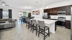 Uma cozinha moderna com armários escuros, eletrodomésticos de aço inoxidável e uma ilha central com banquetas.