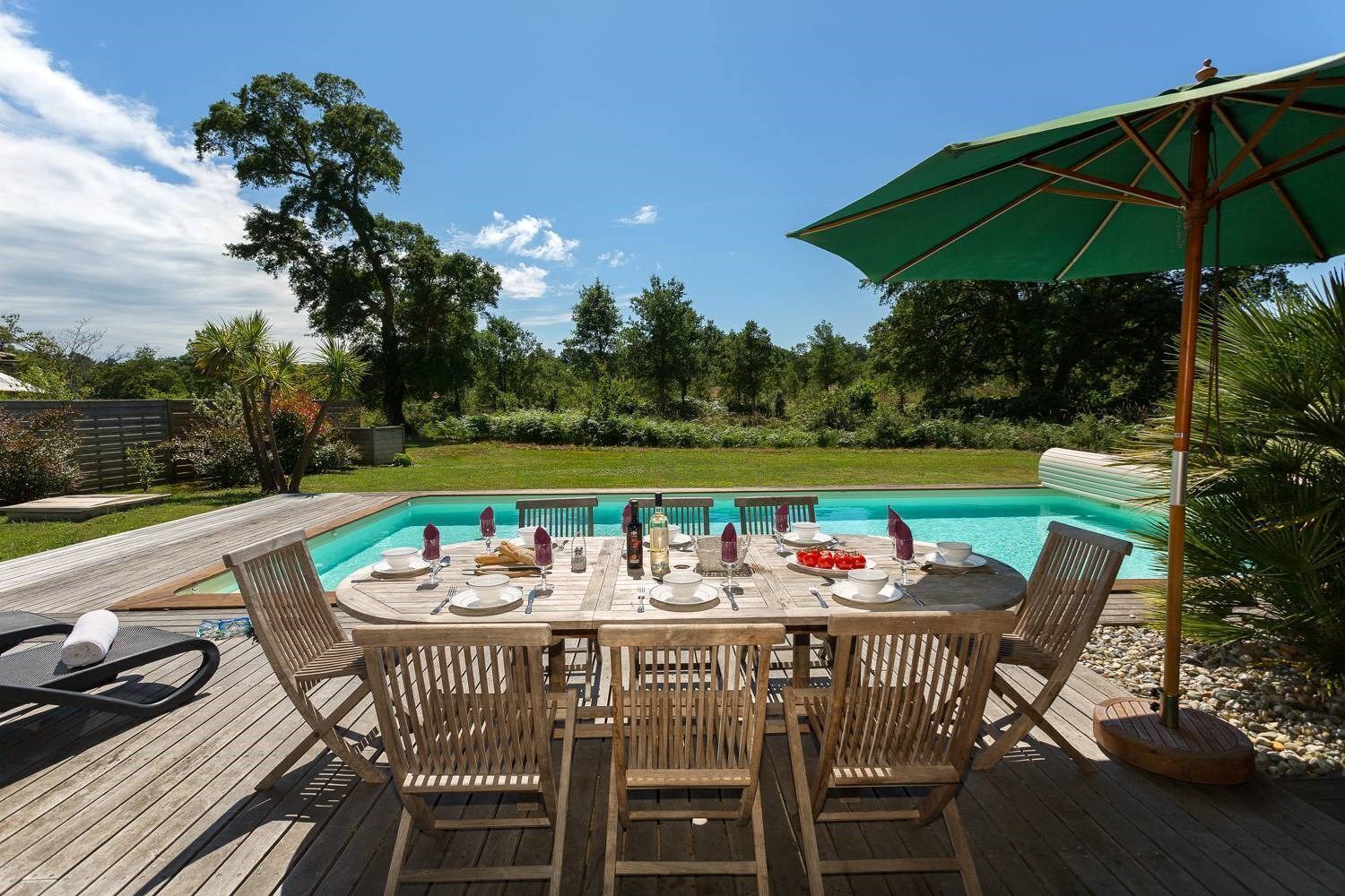 Une terrasse en bois avec une table dressée pour le repas, donnant sur une piscine.