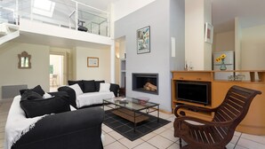 A spacious living area with a high ceiling, a fireplace, a TV, and a balcony. - Belle villa avec piscine privée | Près de la plage (Moliets)