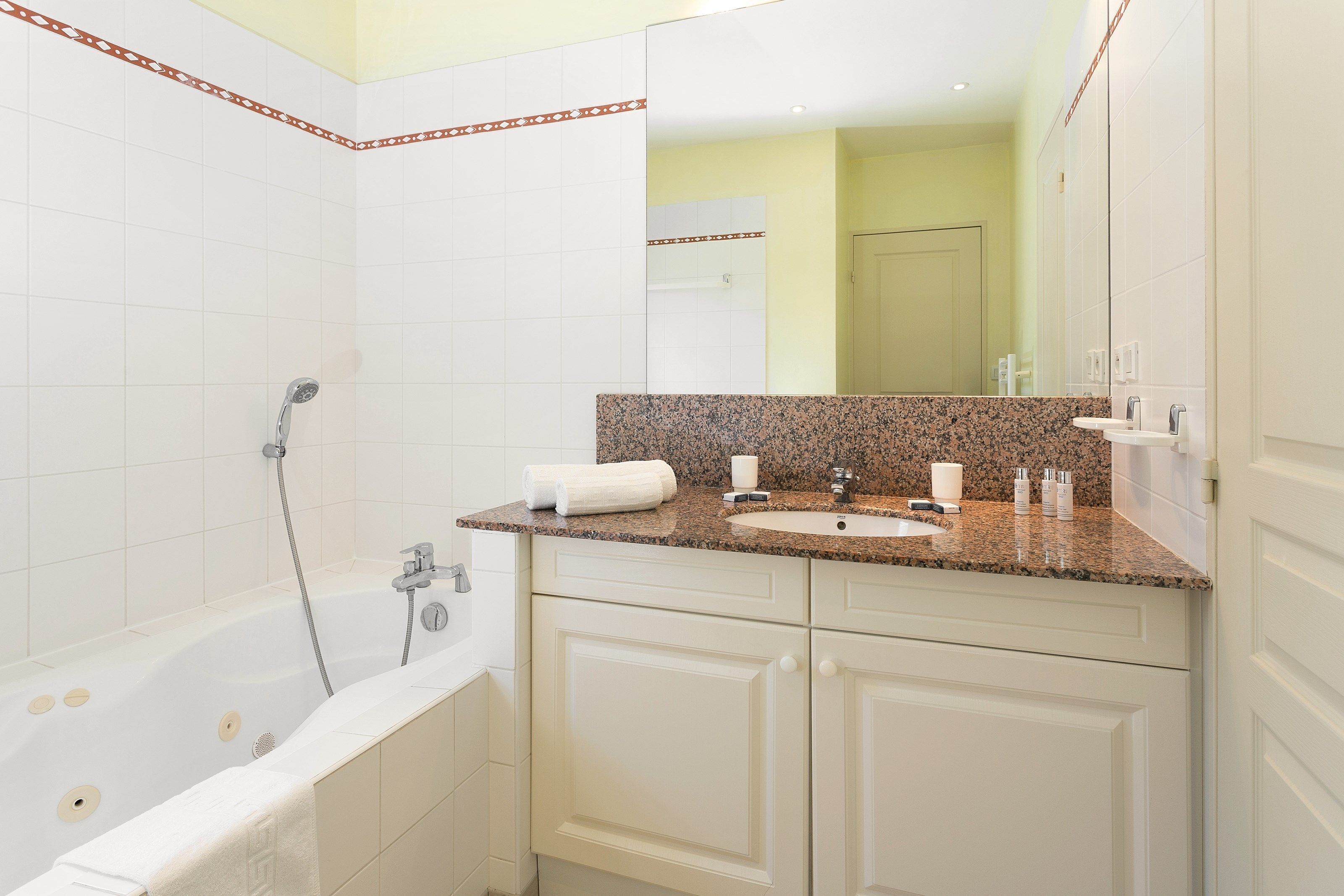 Un baño moderno con una bañera blanca, lavamanos de granito y un espejo grande.