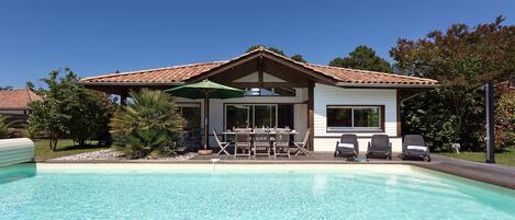 A house with a swimming pool, a patio with chairs, and a covered area with a table and umbrella.