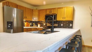 Una cocina con armarios de madera, un refrigerador de acero inoxidable, un grifo negro y una encimera de mármol.
