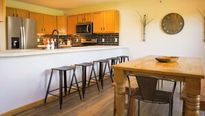 Una cocina moderna con armarios de madera, un refrigerador de acero inoxidable, un microondas y una mesa de comedor de madera con taburetes de bar.