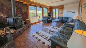 Un salon chaleureux avec une cheminée en pierre, un canapé en cuir et une grande fenêtre donnant sur un paysage magnifique.
