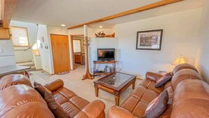 A living room with leather sofas, a glass coffee table, and a television on a stand. - Black Bear Den- Mountain Views - Close to Downtown (Red Lodge)