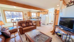 A cozy living room with a leather sofa, a glass coffee table, and a TV on a wooden stand. - Black Bear Den- Mountain Views - Close to Downtown (Red Lodge)