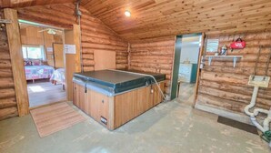 Puuinen mökki, jossa on poreallas, värikkäällä peitteellä varustettu sänky ja pieni keittokomero.