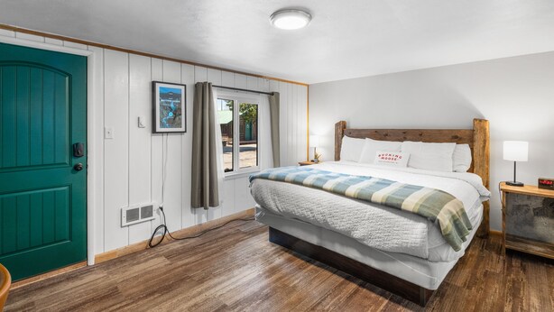 A bedroom with a bed, a wooden headboard, a nightstand, a lamp, and a door.
