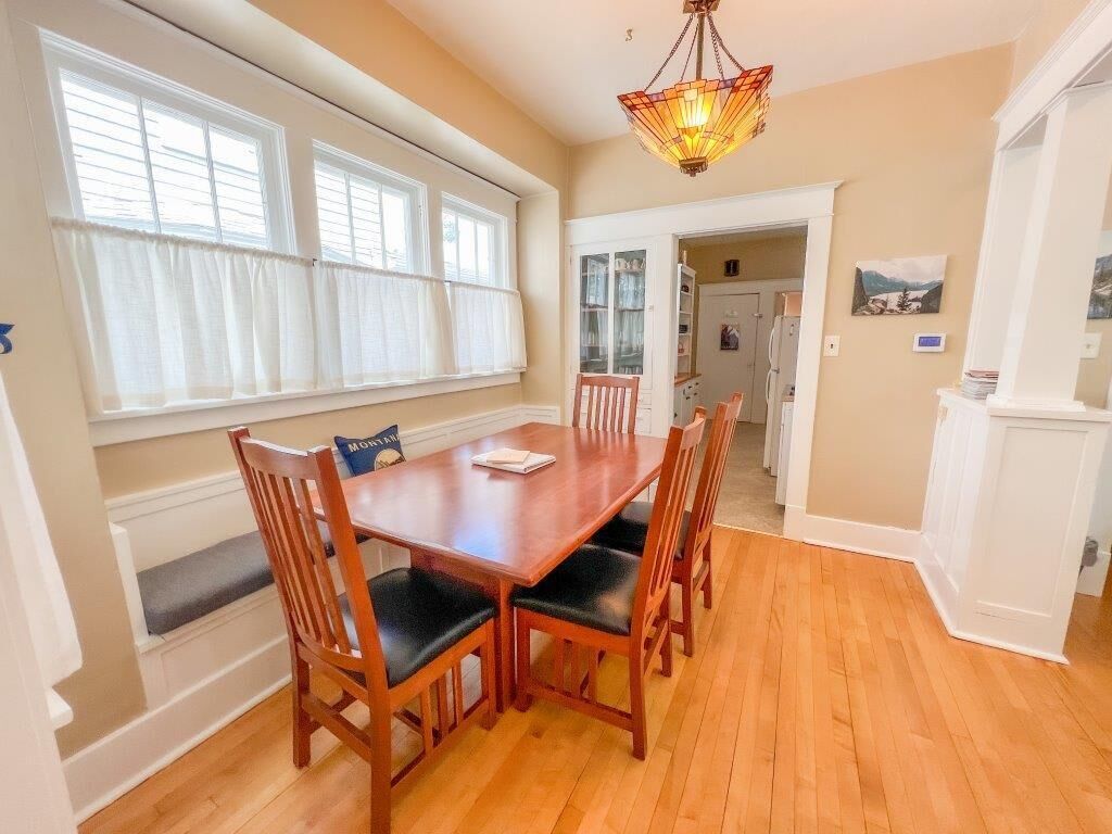 A dining area with a wooden table and chairs, a bench, and a window with curtains.