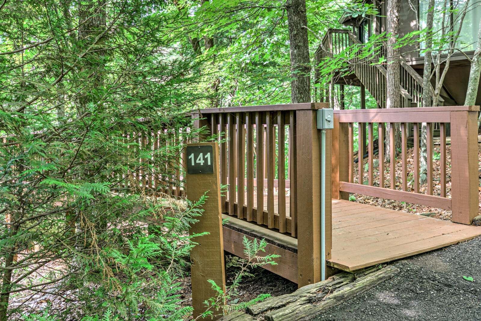 Une terrasse en bois, agrémentée d’une porte en métal, et entourée d’un feuillage verdoyant et luxuriant.